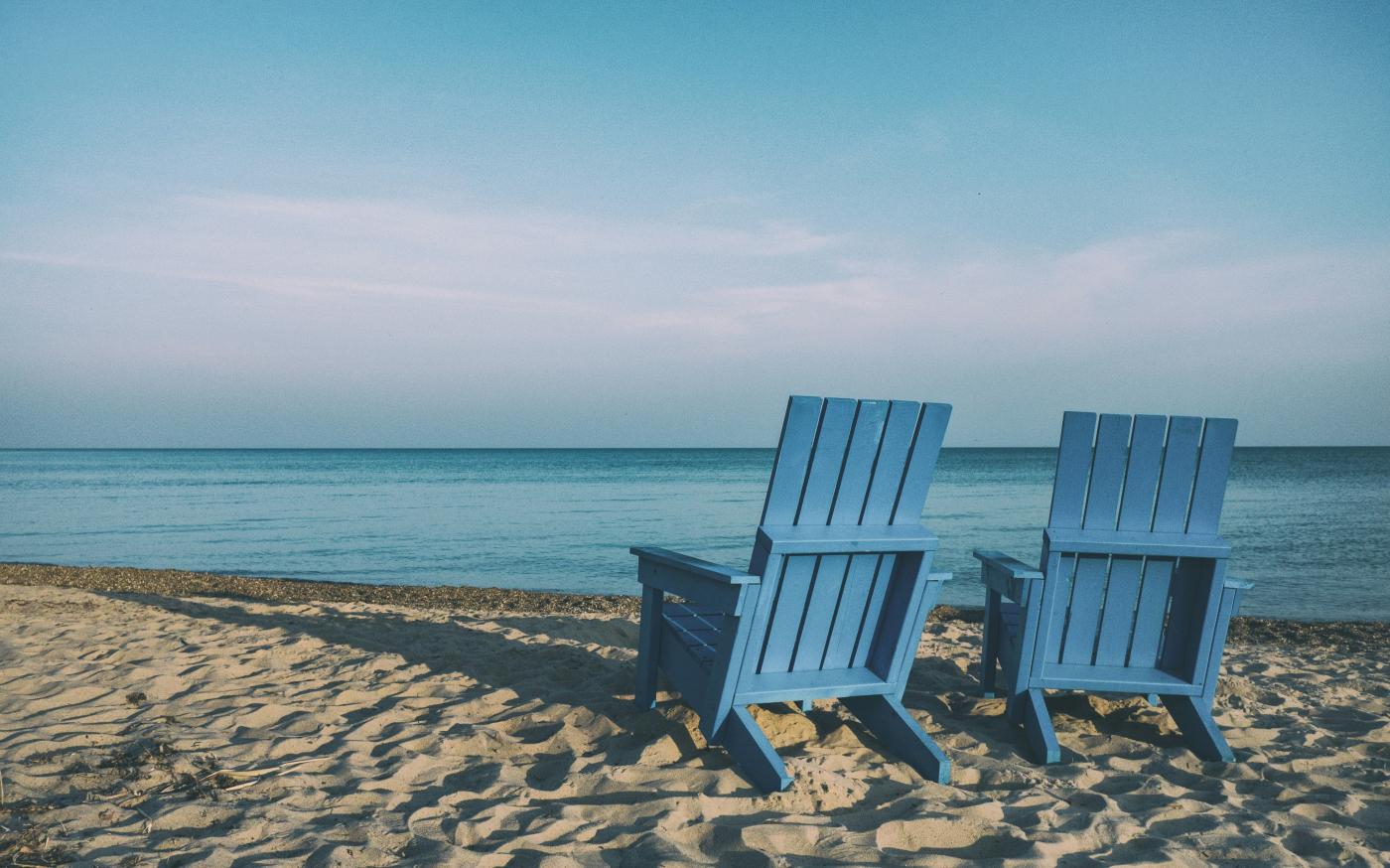 two blue beach chairs near body of water by Aaron Burden courtesy of Unsplash.