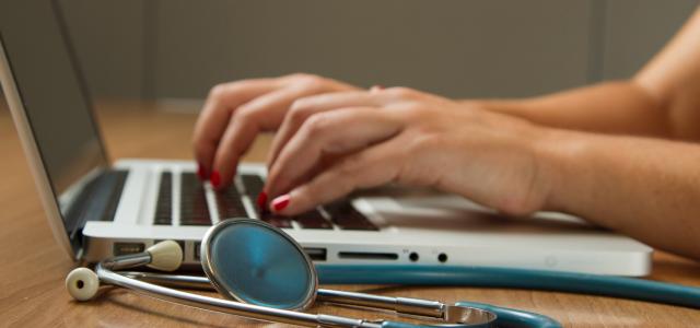 person sitting while using laptop computer and green stethoscope near by National Cancer Institute courtesy of Unsplash.